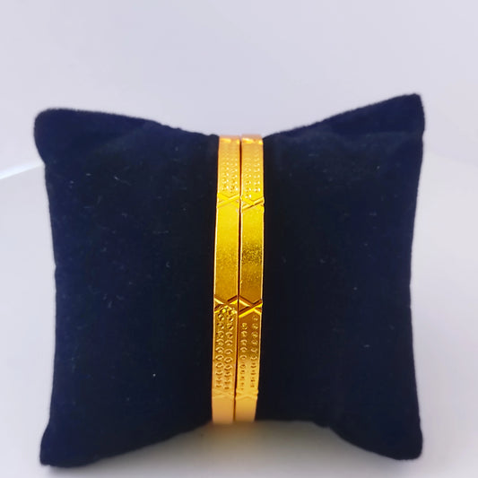 Gold plated bangles on a black cushion against a white background