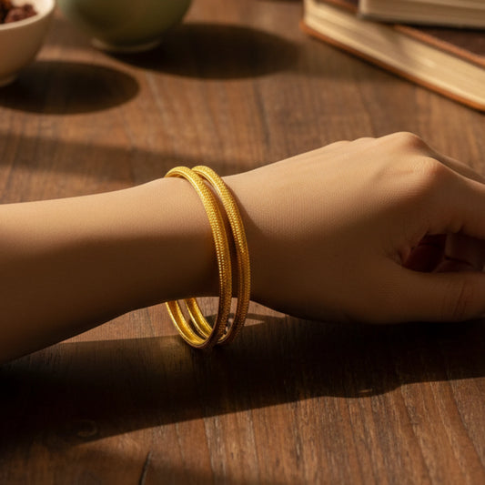 Hand wearing a gold plated classic textured bangles on a wooden surface