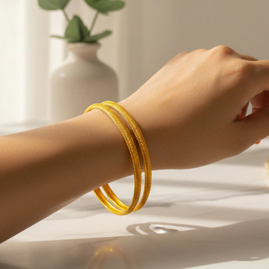 Hand wearing two gold plated bangles with micro texturing on a neutral background