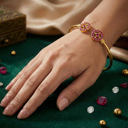 Hand wearing a gold plated bracelet with pink gemstones on a green surface with scattered gemstones.