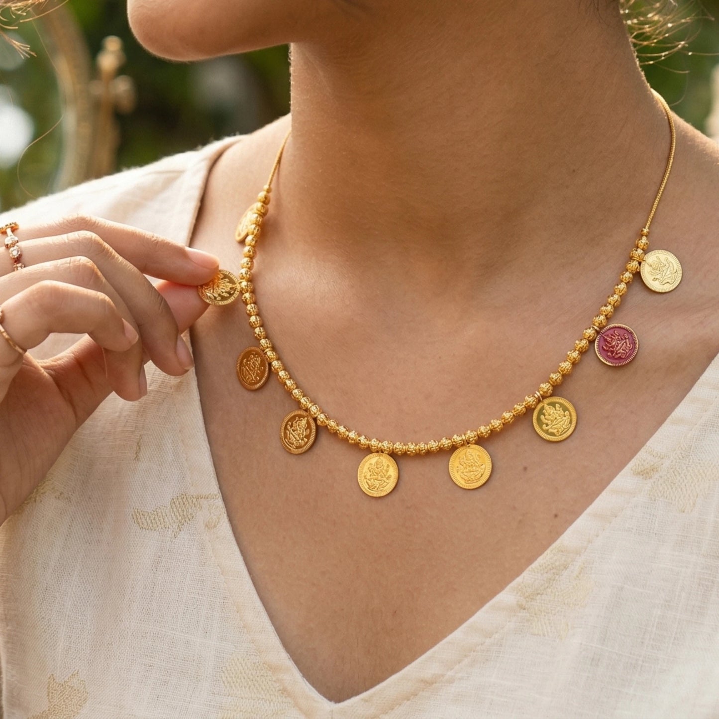 Gold plated choker/necklace with circular lakshmi coin pendants worn by a person, with a blurred natural background