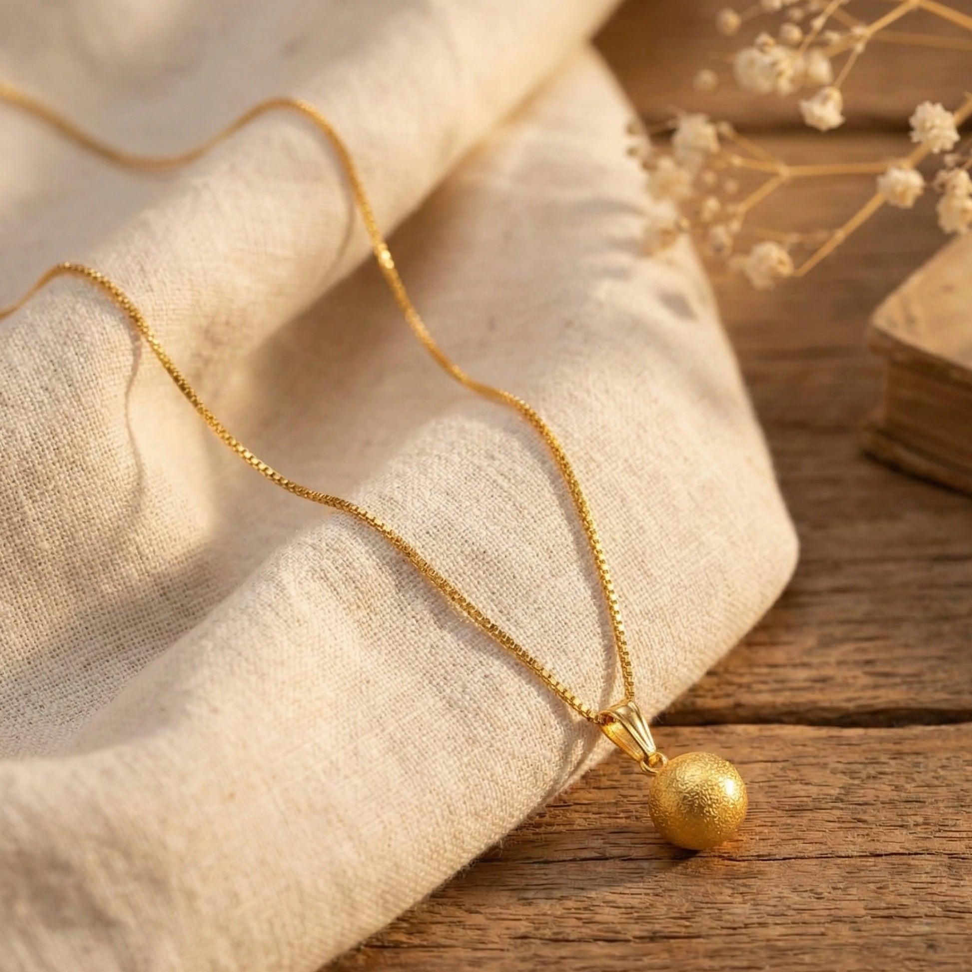 Gold plated necklace with a spherical pendant on a wooden surface