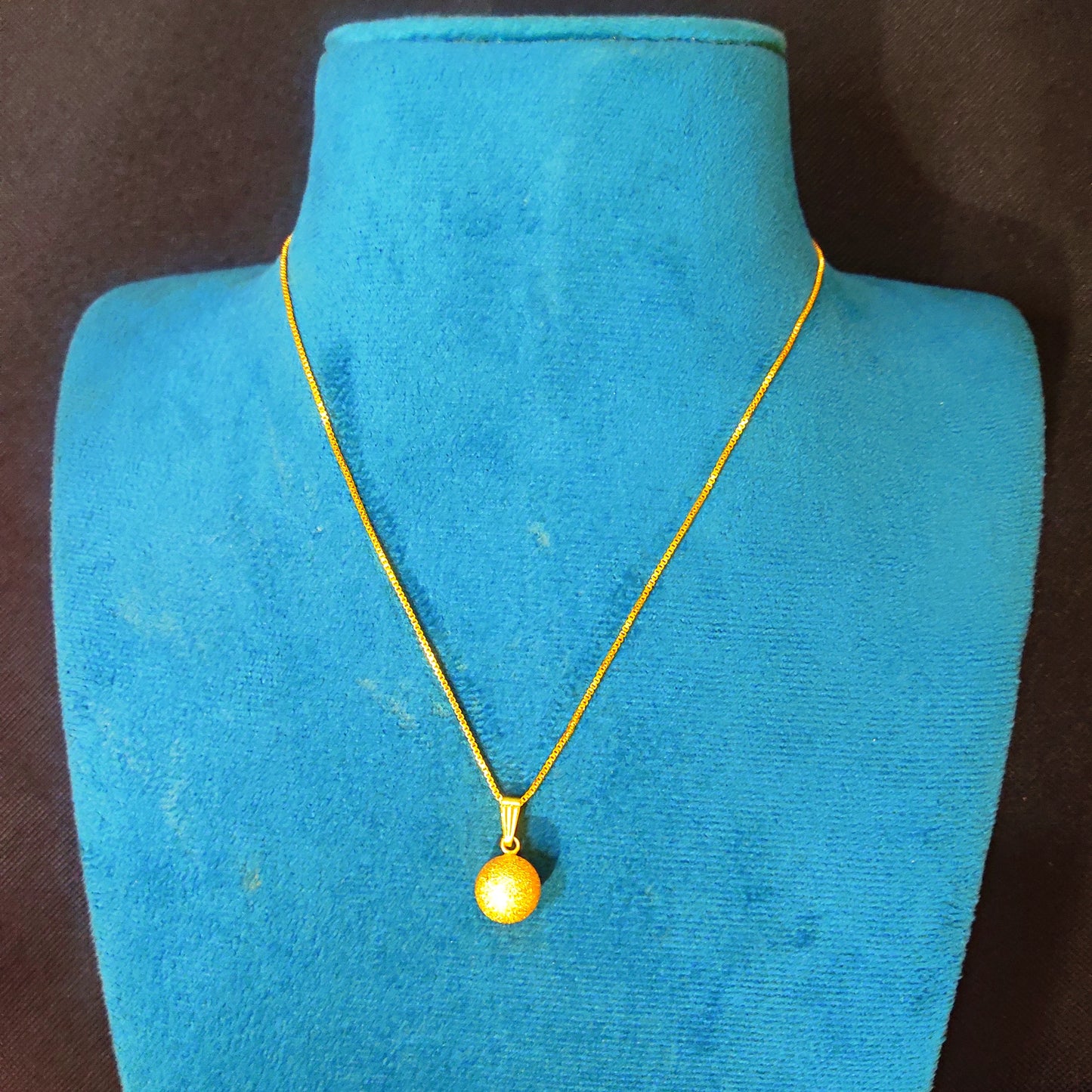 Gold plated necklace with a round pendant on a blue mannequin against a brown background
