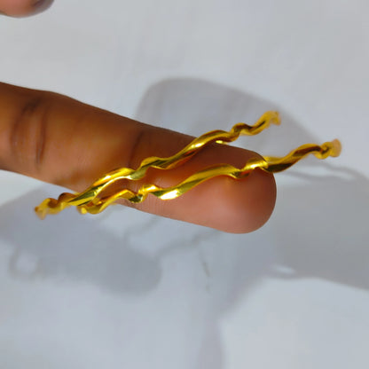 Two Gold Plated Wavy High Shine bangles holded in a finger in a rustic background