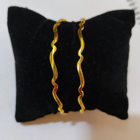 Two gold plated wavy bangles displayed on a black velvet jewelry stand against a white background.