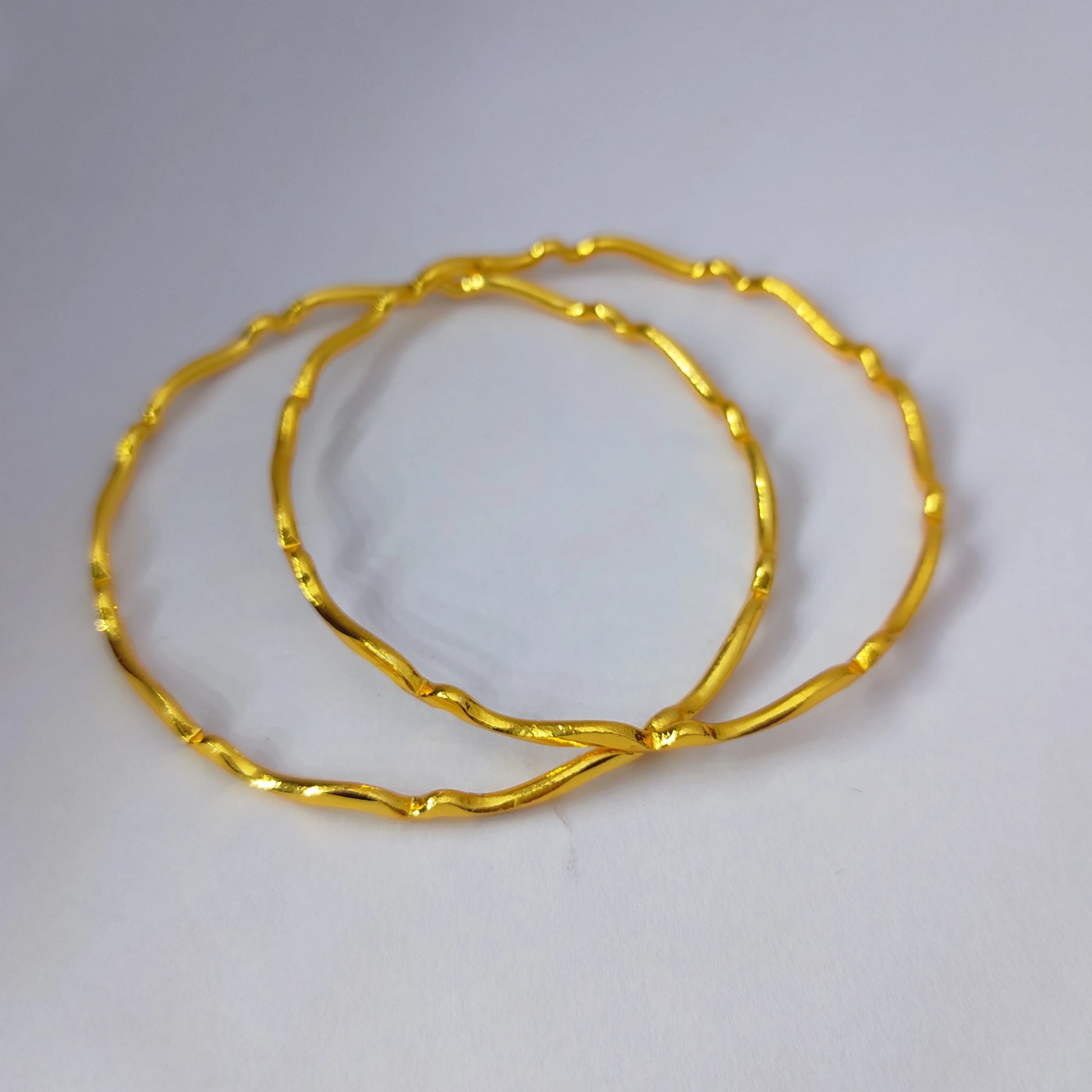 Two Gold Plated wavy design bangles displaced on a white table top