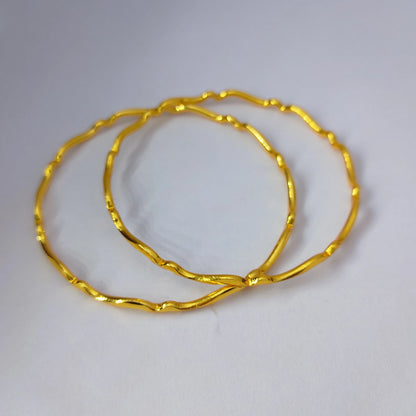 Two Gold Plated wavy design bangles displaced on a white table top