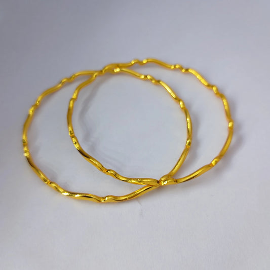 Two Gold Plated wavy design bangles displaced on a white table top
