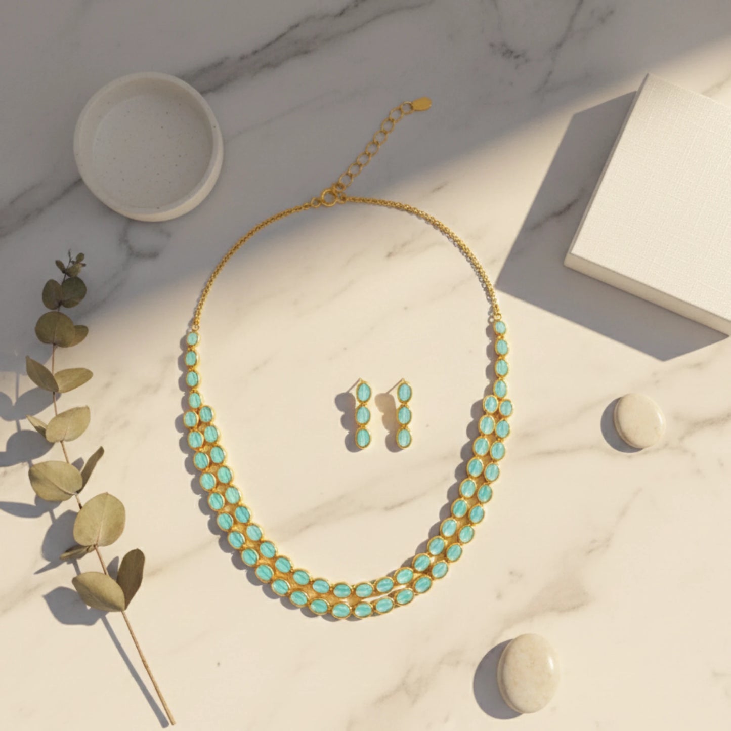 Gold plated necklace with turquoise stones and matching earrings on a marble surface.