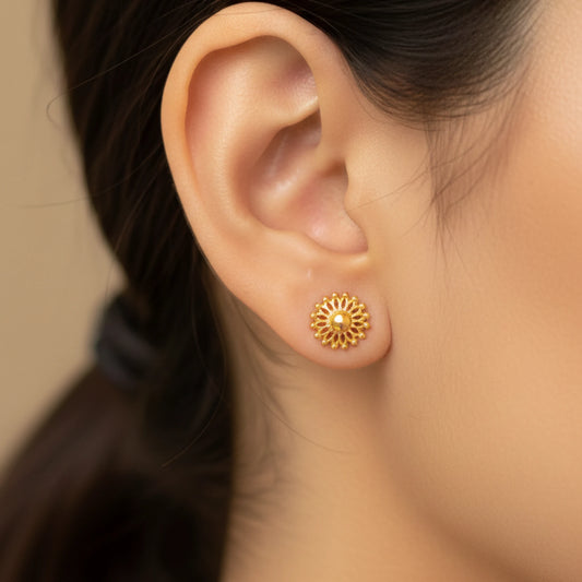 Gold plated floral earring worn by a person with a blurred background