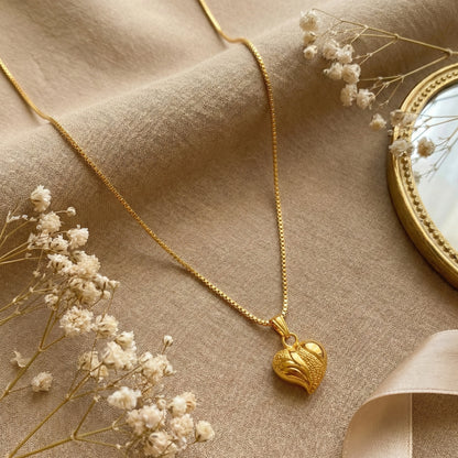 Gold plated neckchain with a heart pendant on a beige fabric background with dried flowers.