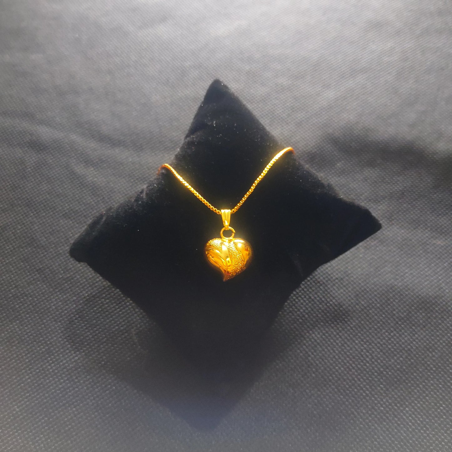 Gold plated heart-shaped pendant on a black cushion against a gray background