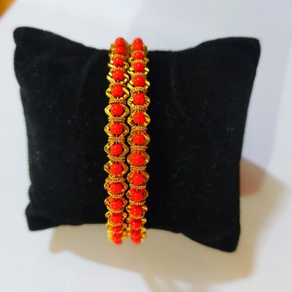 Two gold plated coral beaded bangles displayed on a black velvet jewelry stand against a white background.