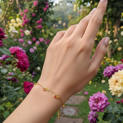Hand wearing a gold plated bracelet with ruby red heart charms and flowers in the background