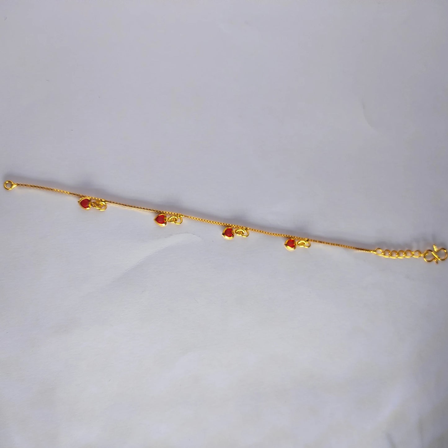Gold plated bracelet with ruby red heart charms on a light gray background