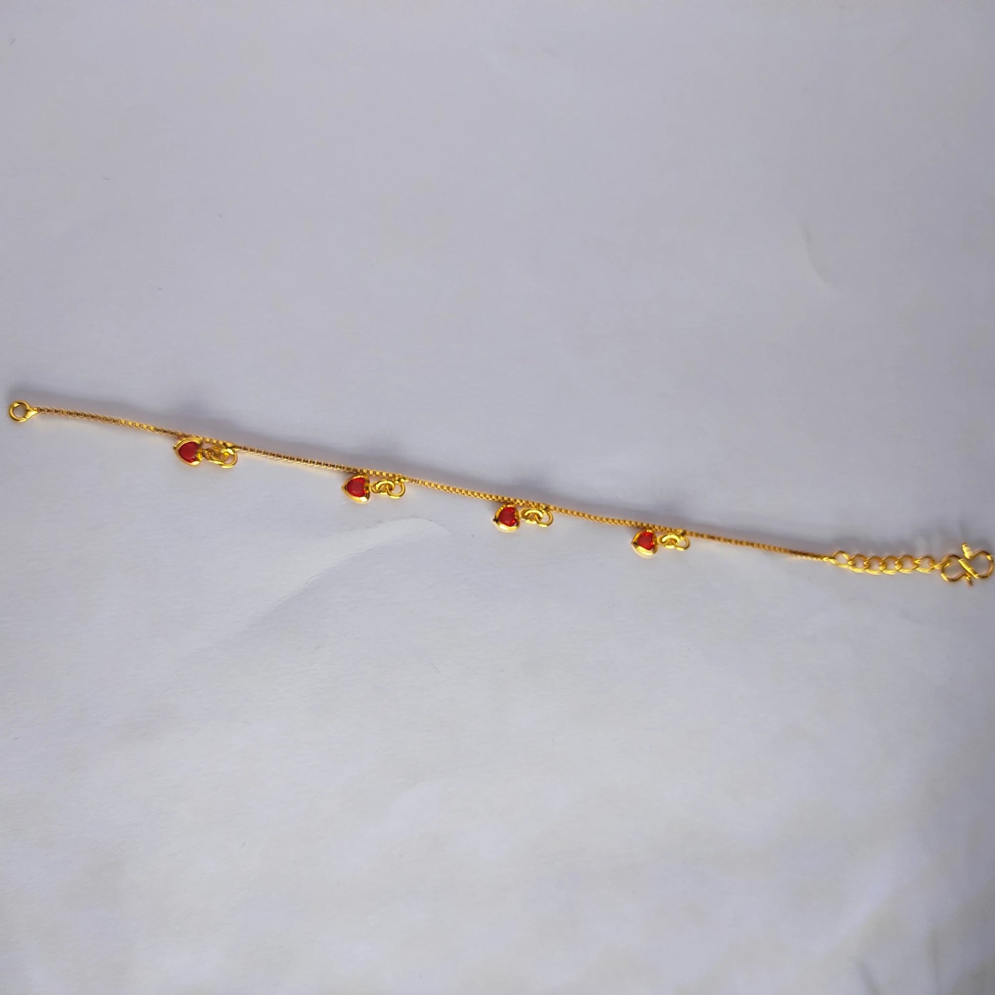 Gold plated bracelet with ruby red heart charms on a light gray background
