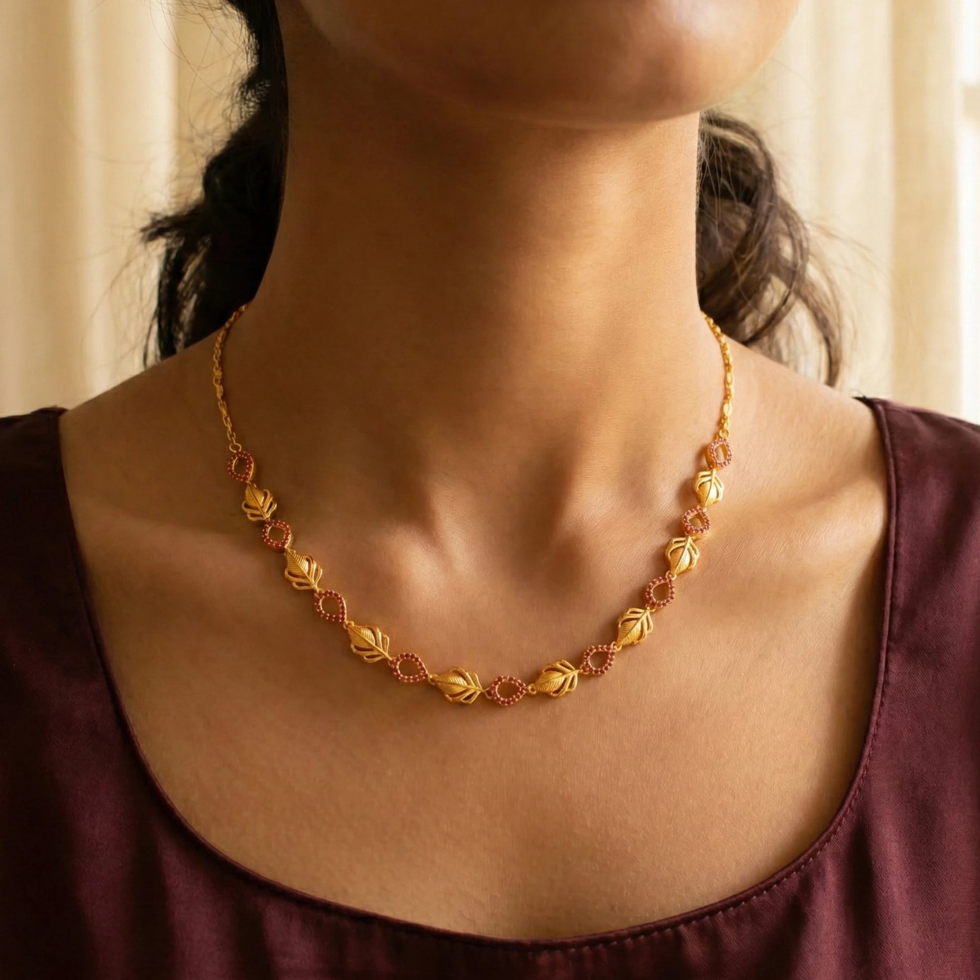 Gold plated necklace worn by a person with a neutral background