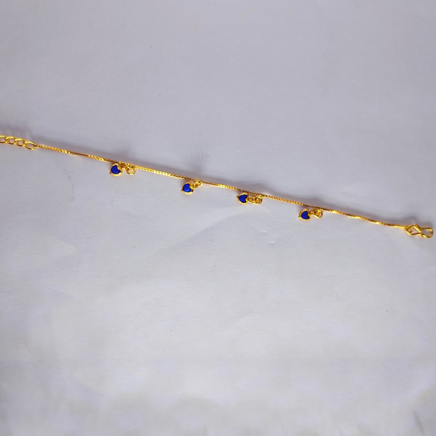 Gold plated bracelet with blue heart charm stones on a light gray background