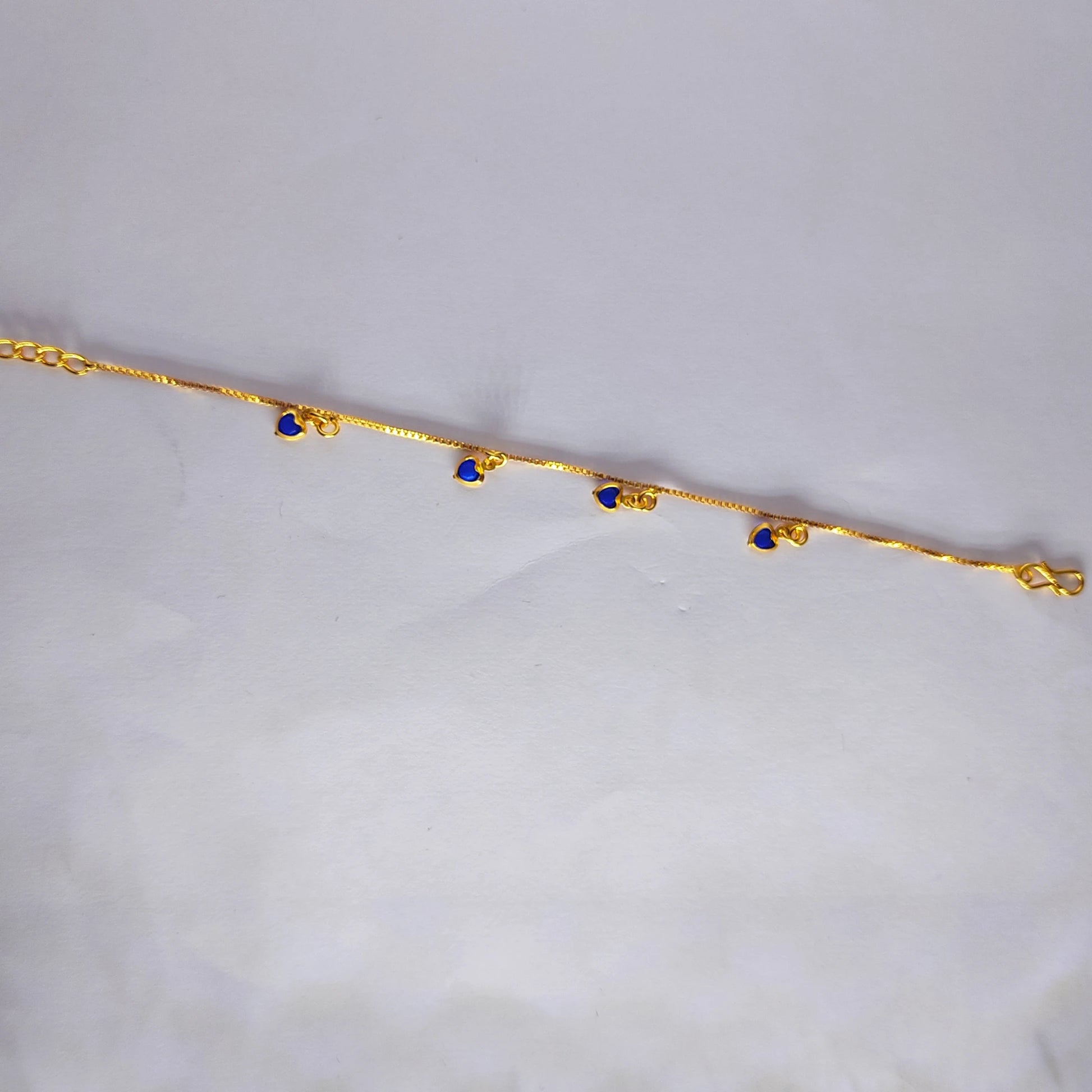 Gold plated bracelet with blue heart charm stones on a light gray background