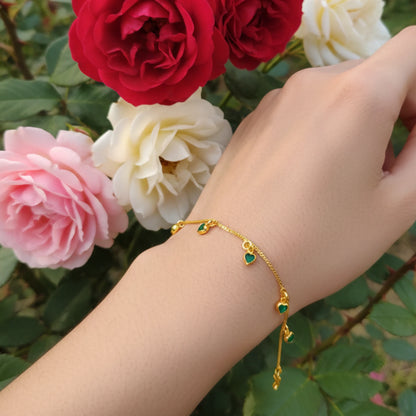 Gold plated bracelet with green heart charms stones on a wrist against a background of red and pink roses.