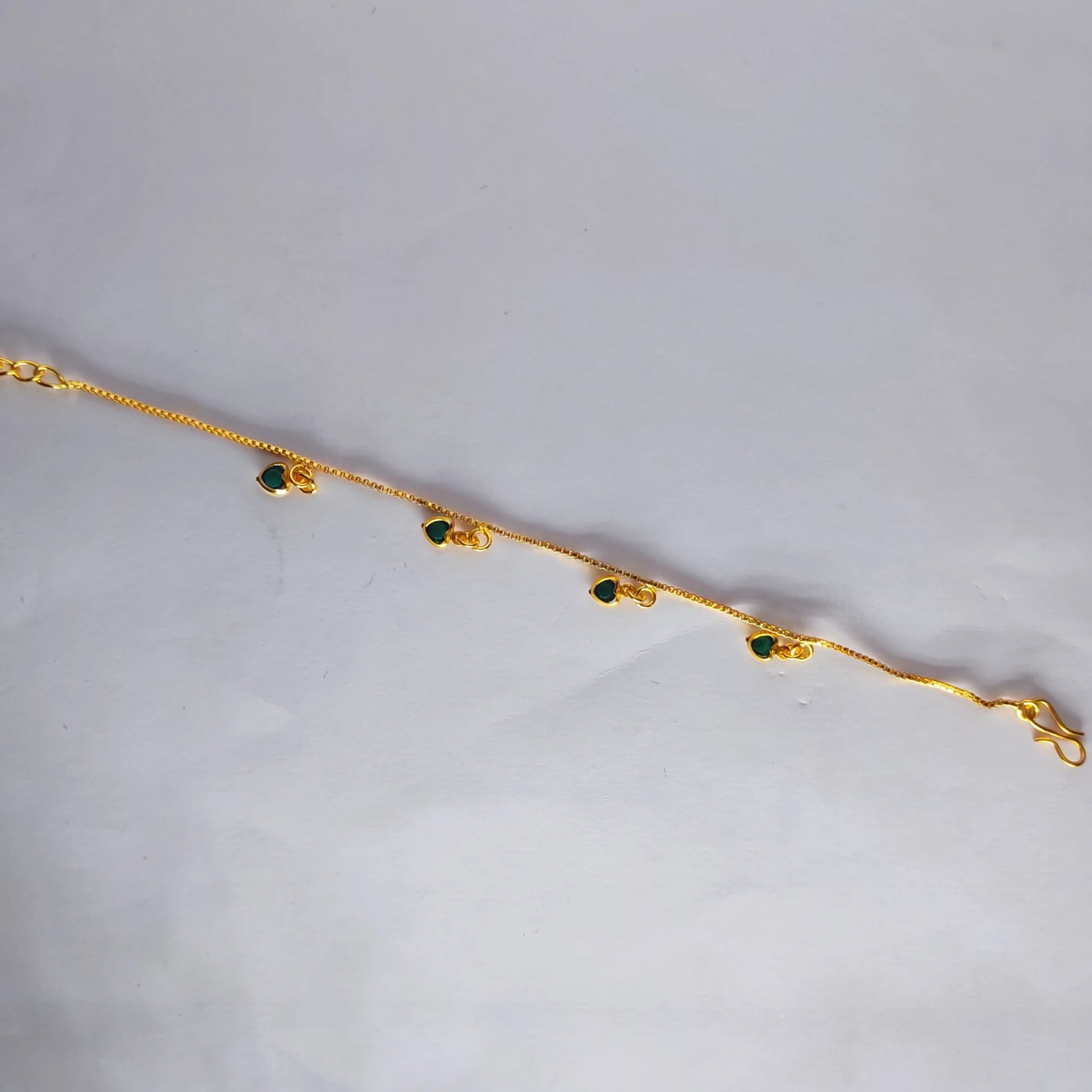Gold plated bracelet with green heart charm stones on a light gray background