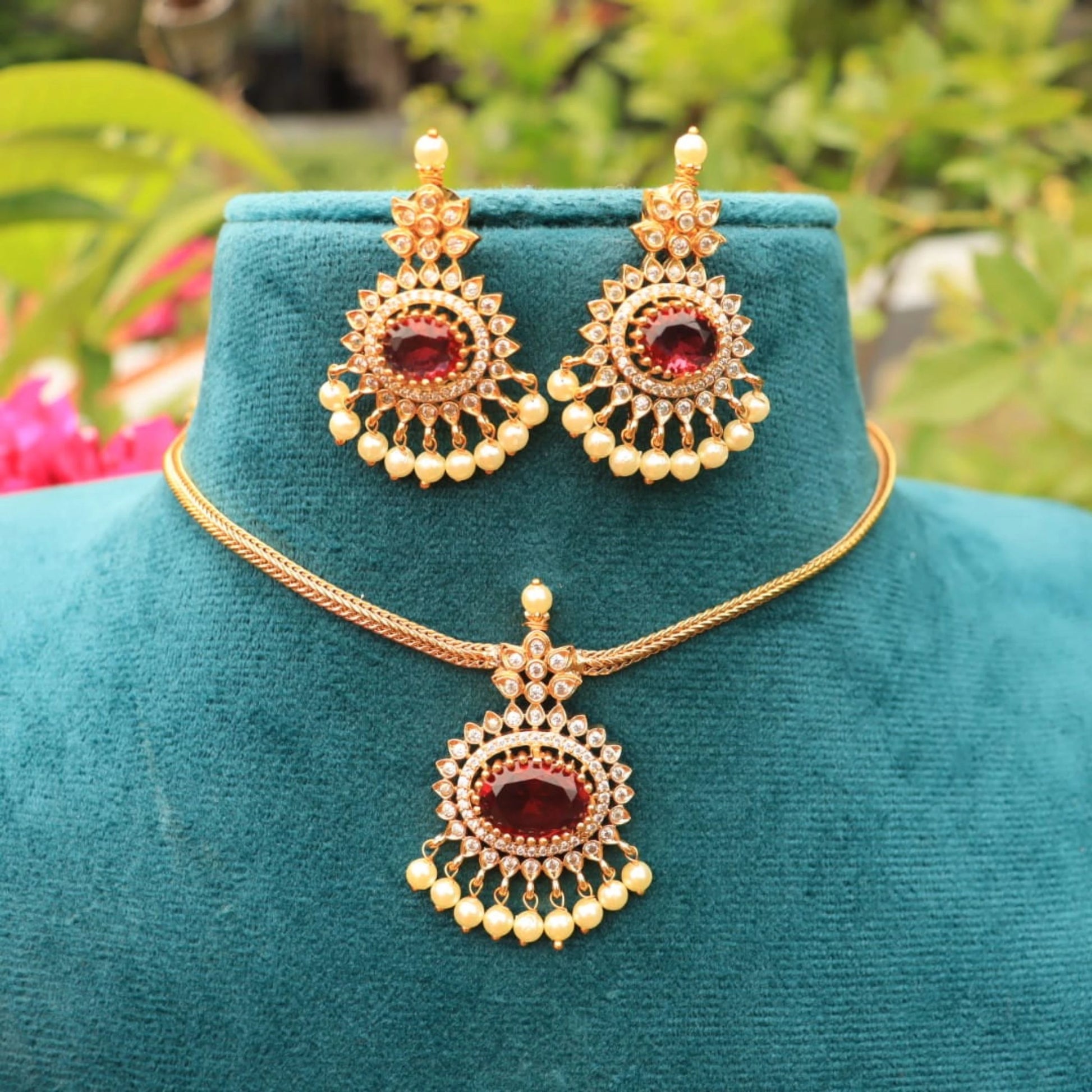 Gold toned necklace and earrings set on a teal mannequin with a blurred natural background