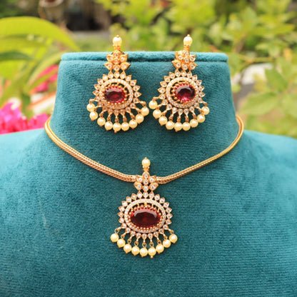 Gold toned necklace and earrings set on a teal mannequin with a blurred natural background