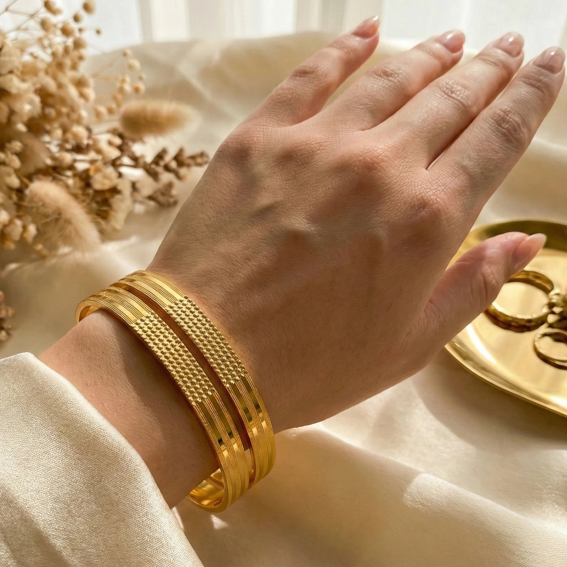 Hand wearing a gold plated set of bangles with a soft, blurred background