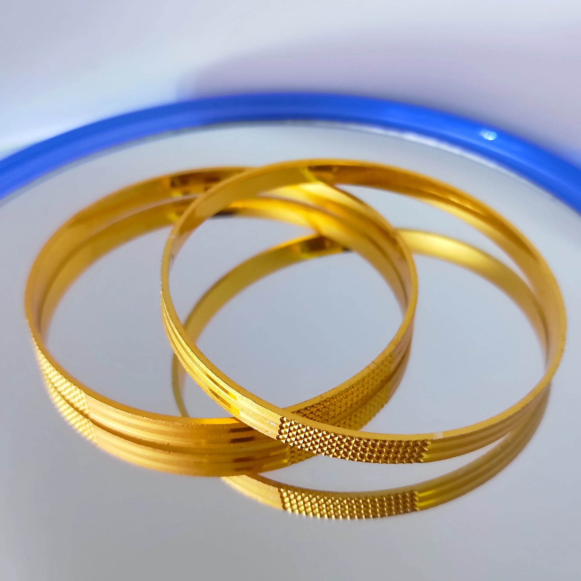 Two gold plated bangles on a white background with a blue rim.