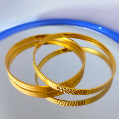 Two gold plated bangles on a white background with a blue rim.