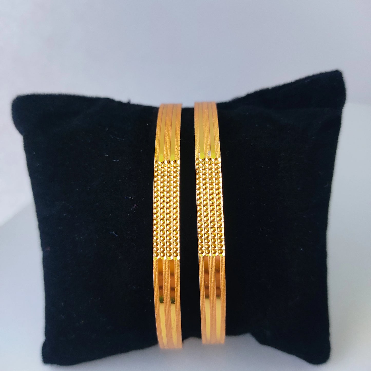 Two gold plated bangles on a black cushion against a white background