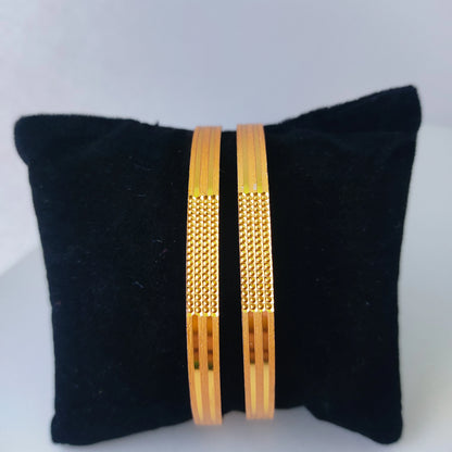 Two gold plated bangles on a black cushion against a white background