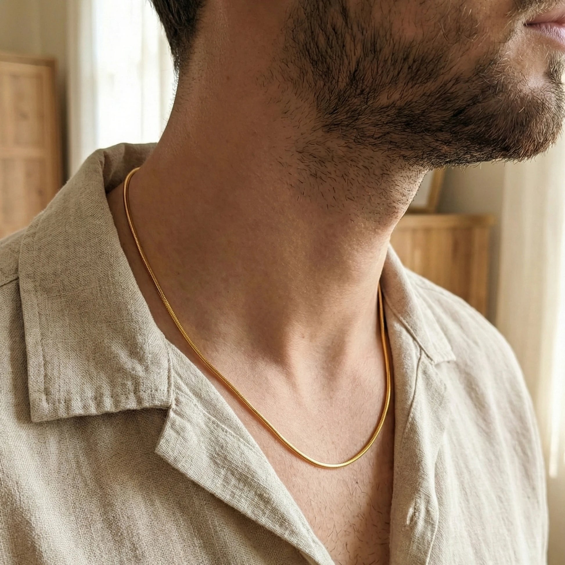 Man wearing a gold plated neckchain with a neutral background