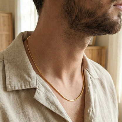 Man wearing a gold plated neckchain with a neutral background