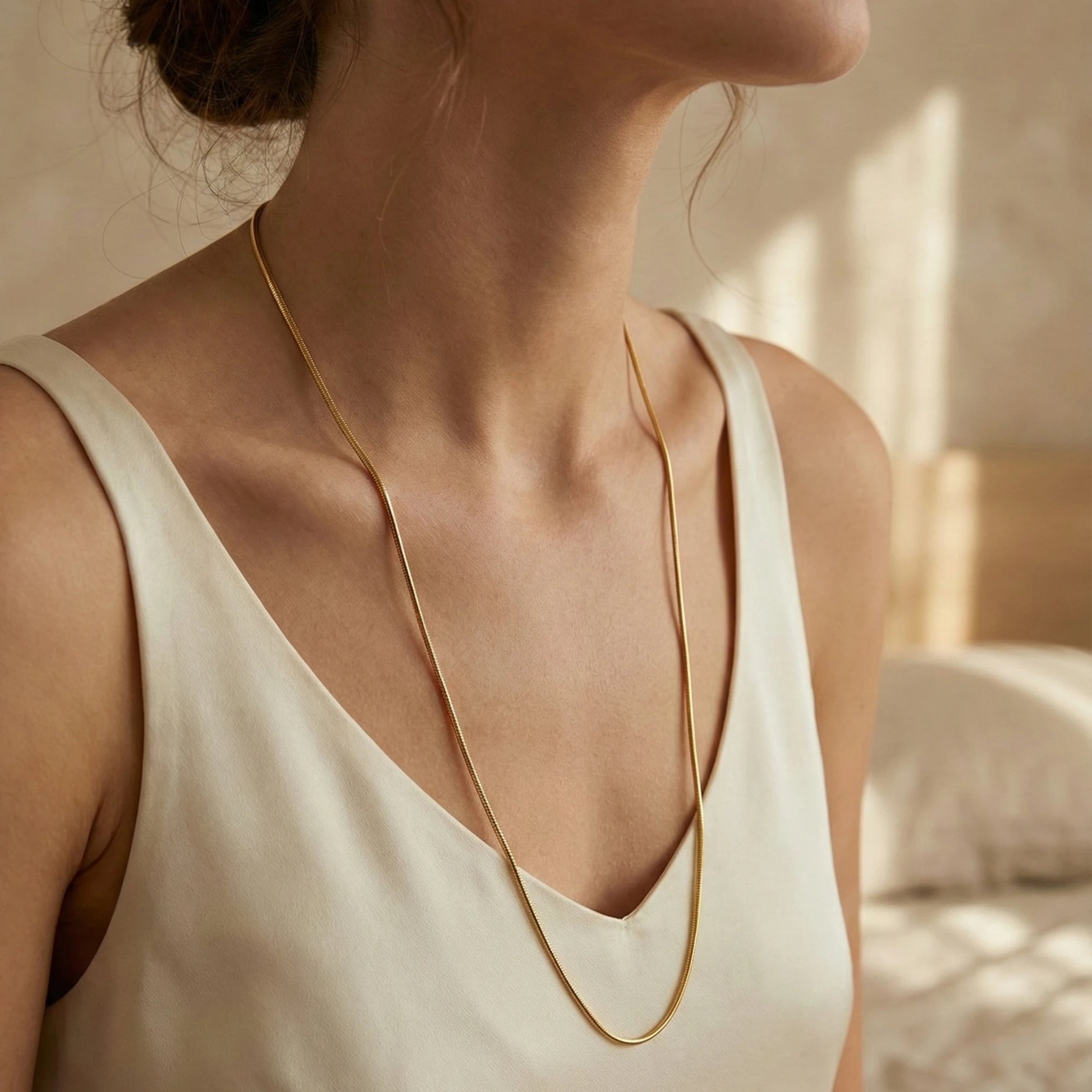 Woman wearing a gold plated neckchain with a neutral background