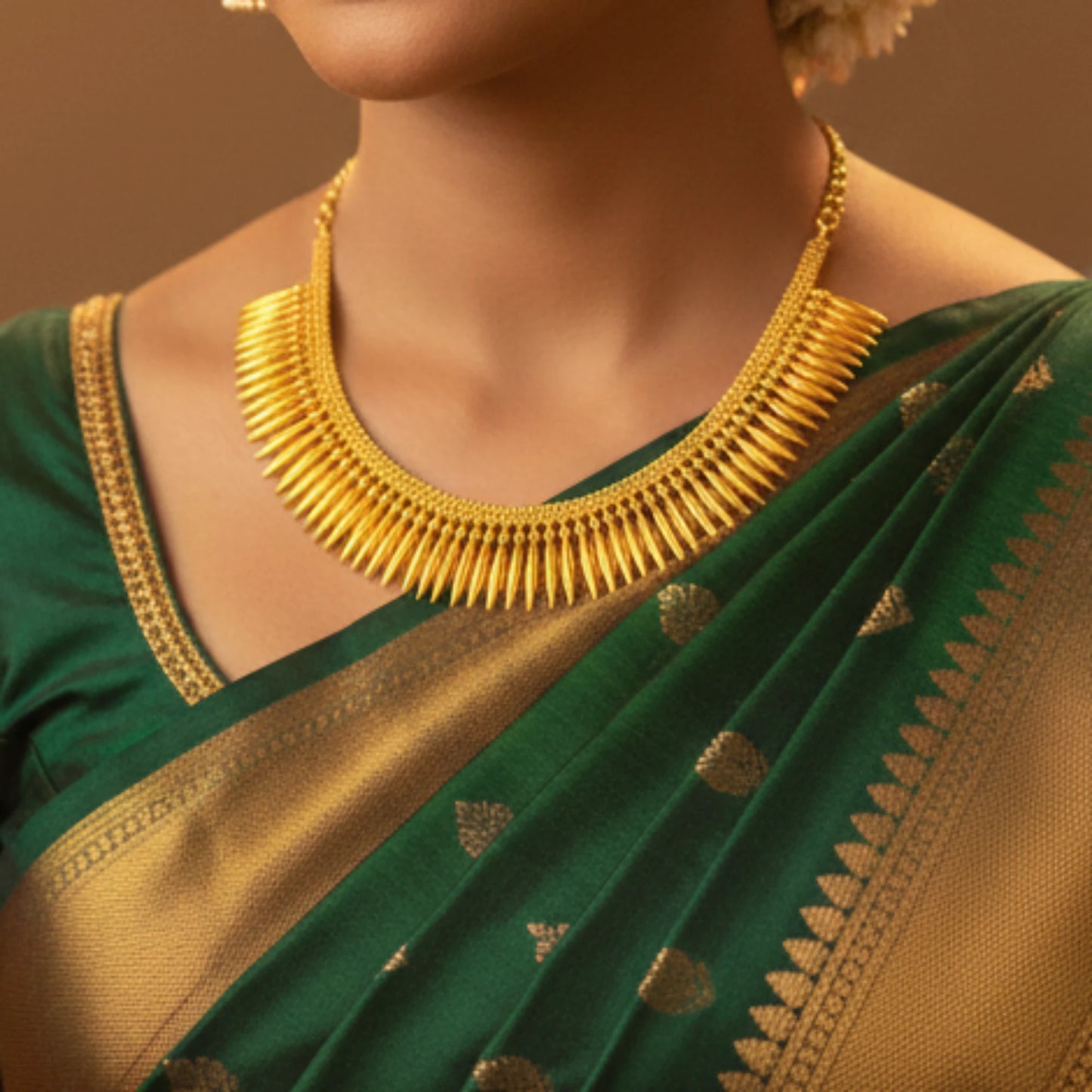 Woman wearing a green saree with gold patterns and a gold plated necklace against a brown background
