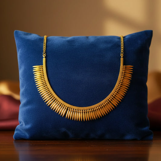 Gold plated Mulla Mottu necklace on a blue pillow with a blurred background