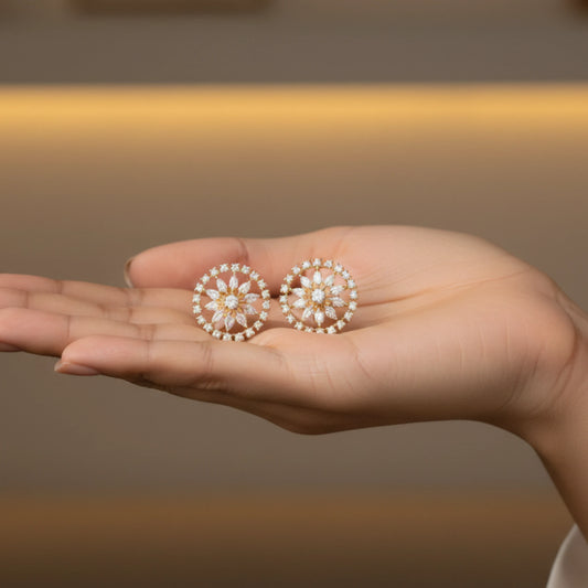Hand holding two decorative gold plated sparkling marquise crystal floral earrings against a blurred background