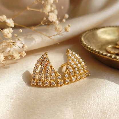 Gold plated earrings with AD accents on a beige surface with dried flowers.