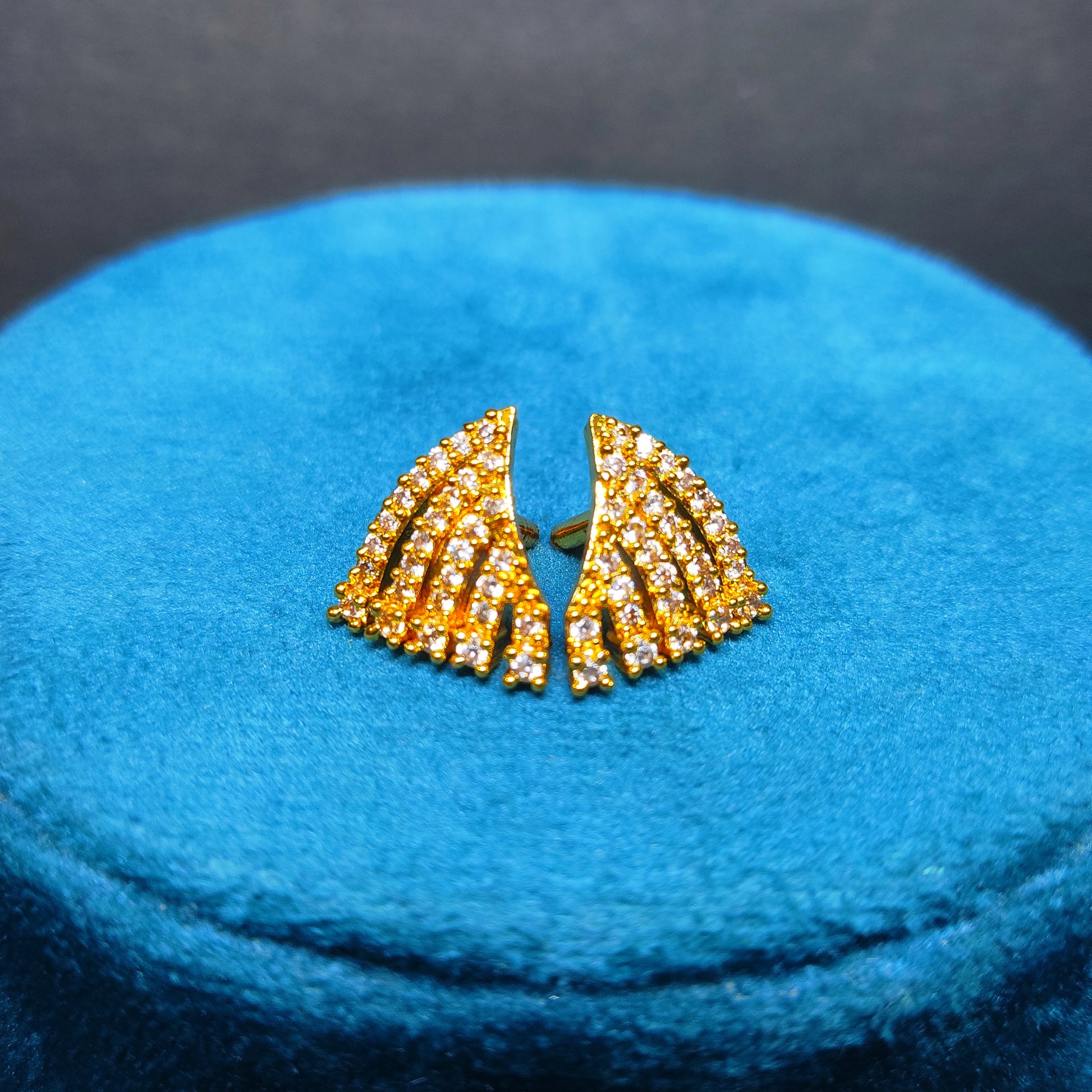 Gold plated earrings with gemstones on a blue cushion