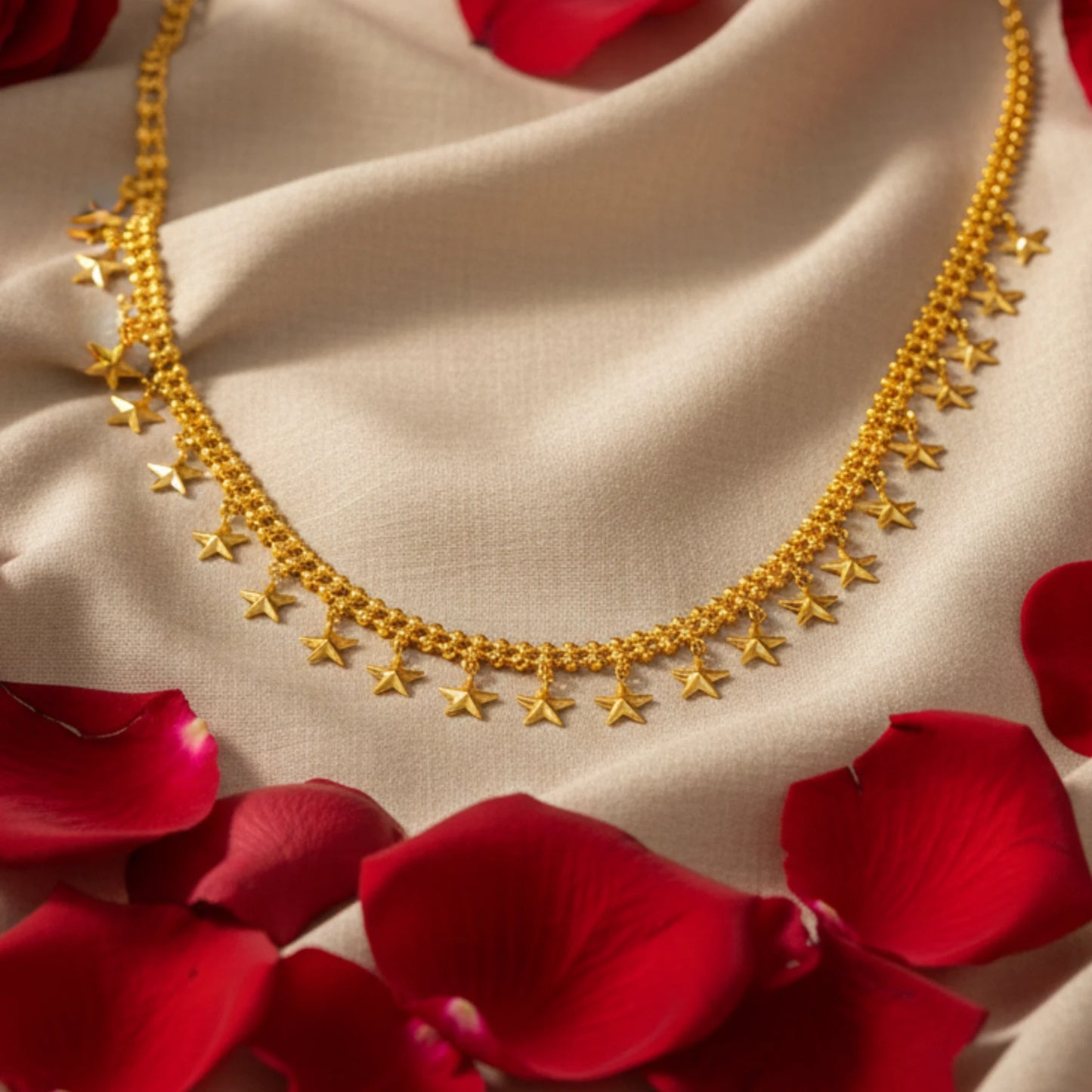 Gold plated necklace with star designs charms or pendants on a beige fabric background with red rose petals.