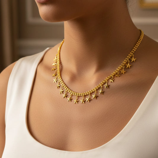 Gold plated necklace with star pendants on a person wearing a white top.