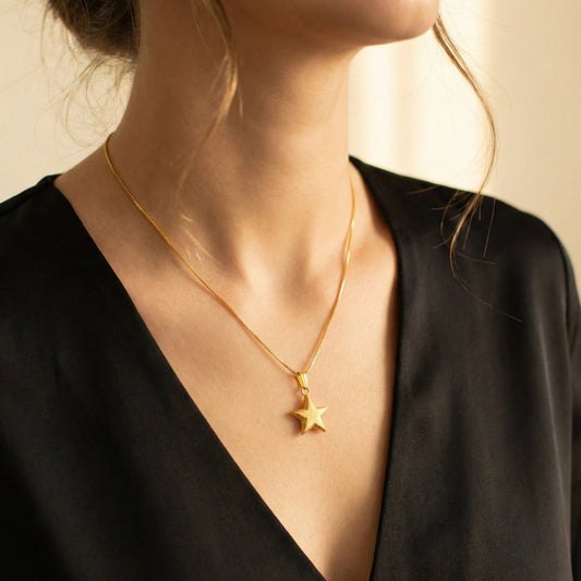 Gold plated star necklace on a person wearing a black top against a beige background