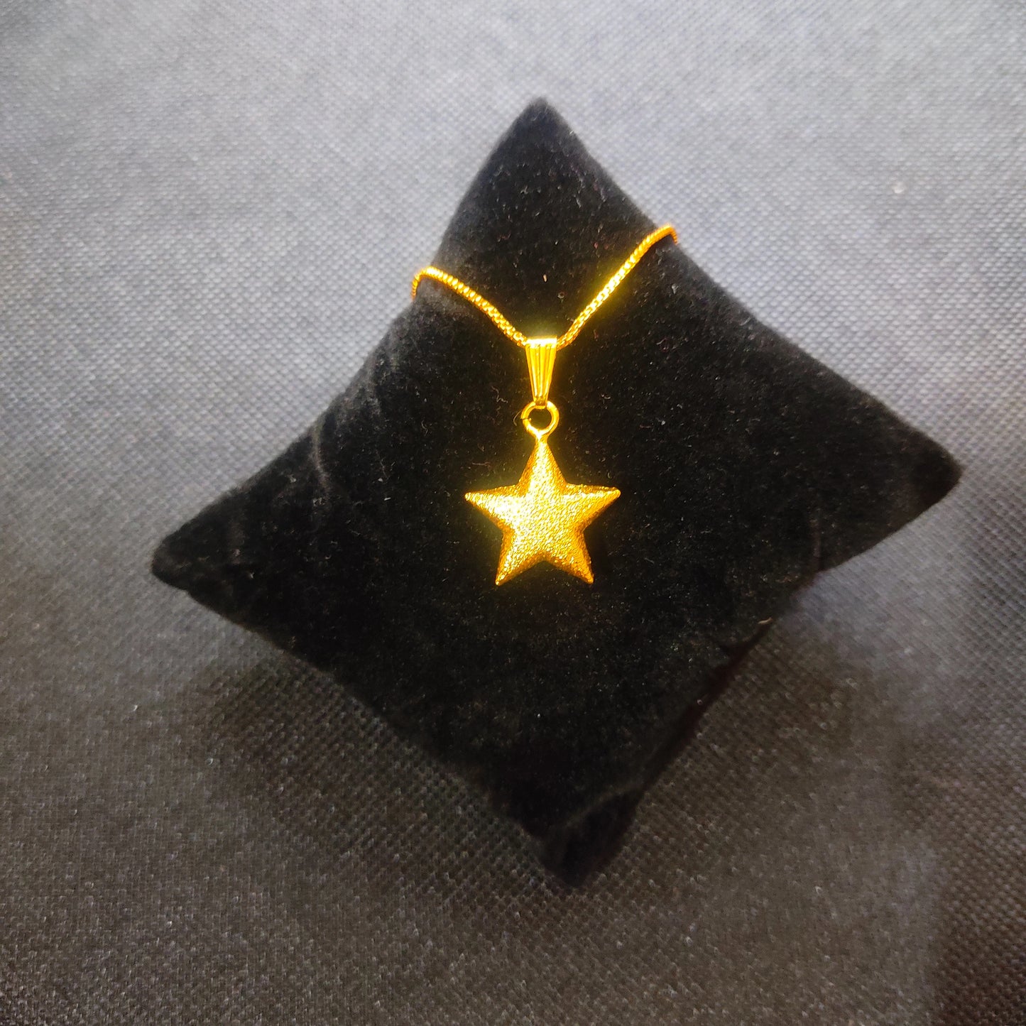 Gold plated star-shaped pendant on a black cushion against a gray background