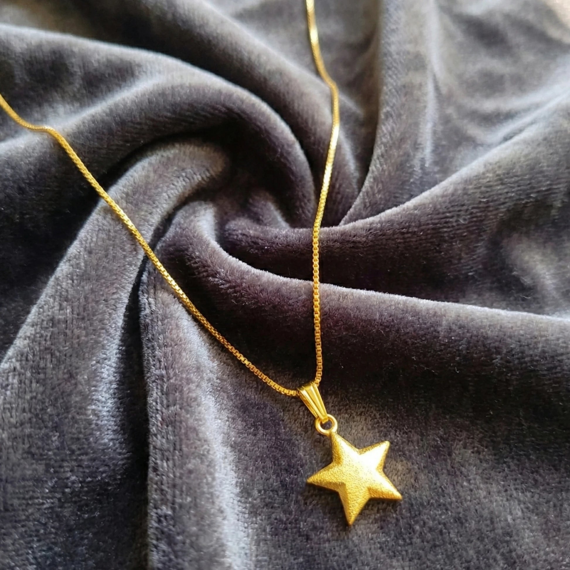 Gold plated star pendant necklace on a textured gray fabric background