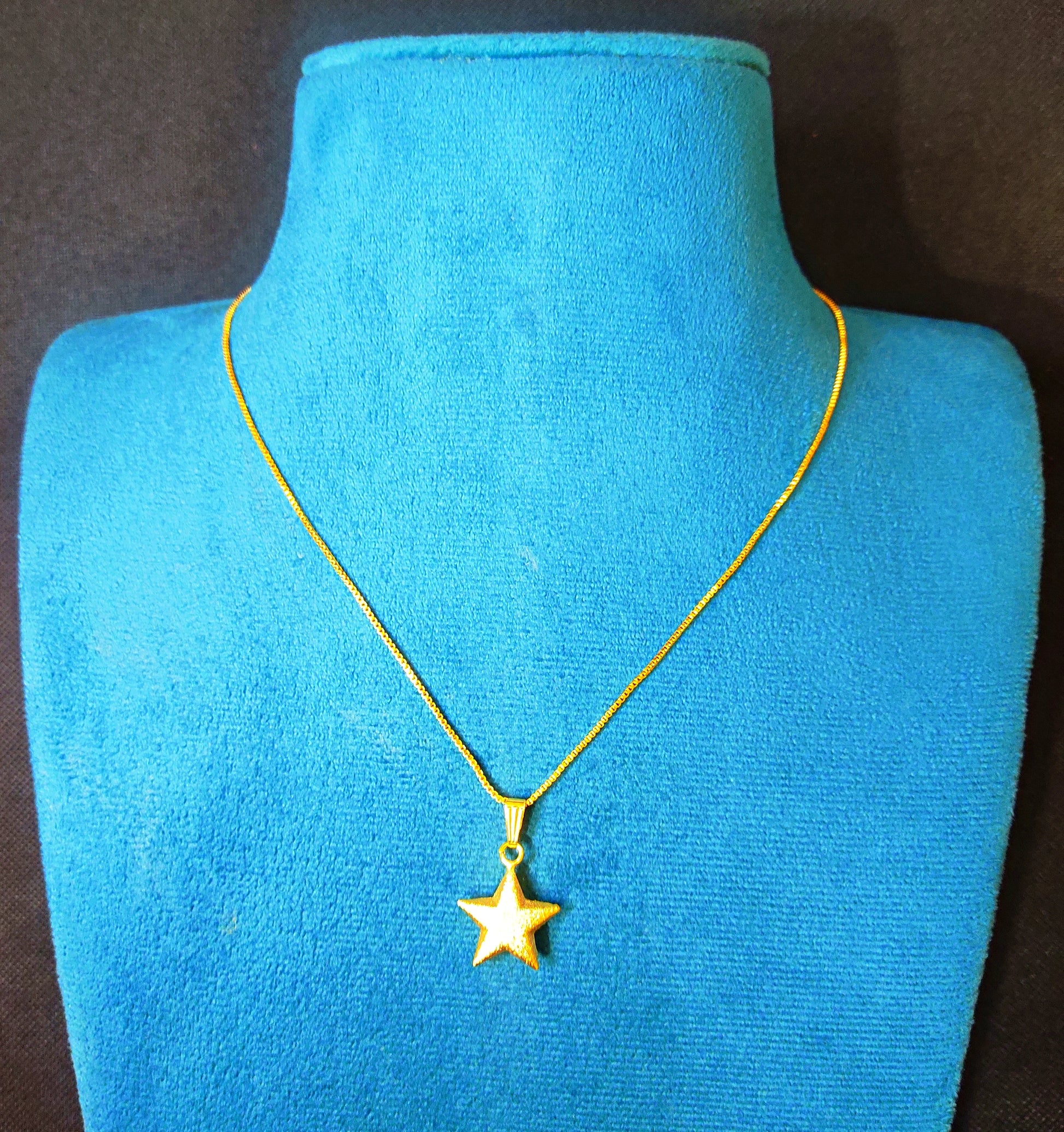 Gold plated star necklace on a blue mannequin against a black background