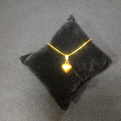 Gold plated neckchain with a heart pendant on a black pillow against a gray background