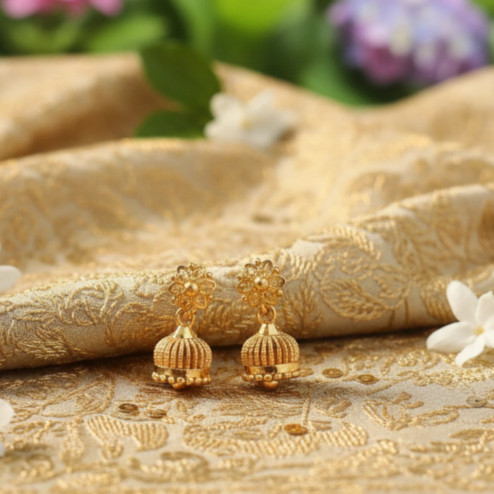 Gold plated Jimikki earrings on a textured gold fabric background with flowers.
