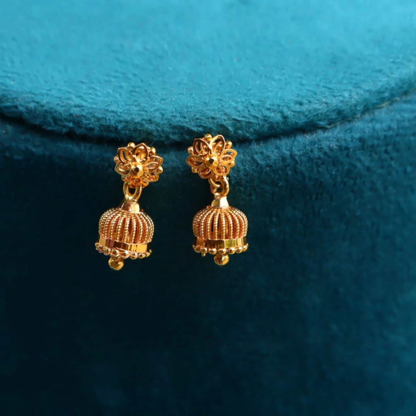 Pair of gold-plated Jimikki earrings on a teal fabric background
