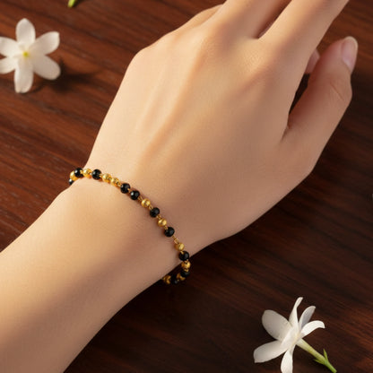 Hand wearing a black beaded gold plated bracelet on a wooden surface with white flowers.